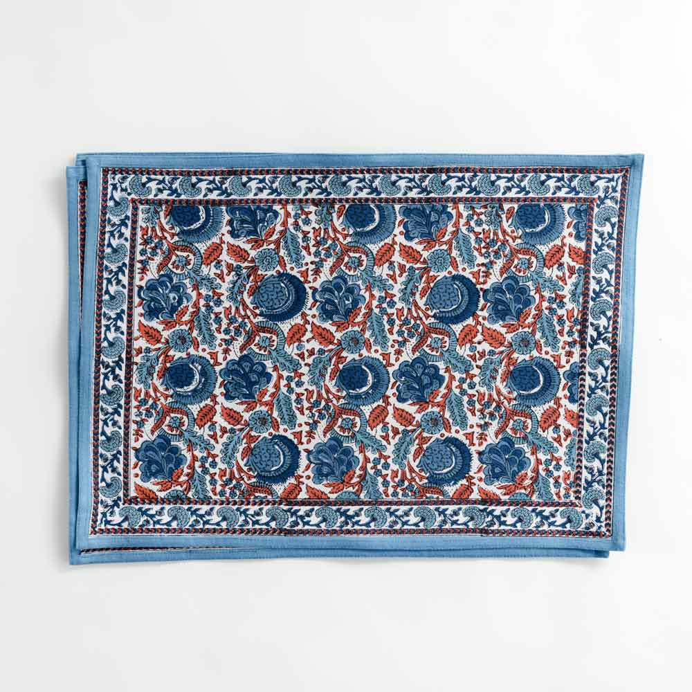 Floral pattern placemat with different hues of blues and paprika orange. 