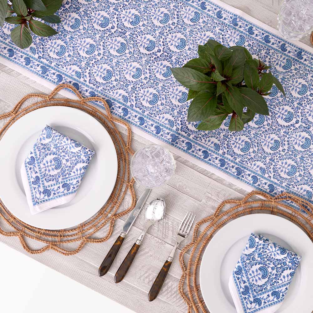 Table runner paired with matching napkin set on dinner table with greenery. 