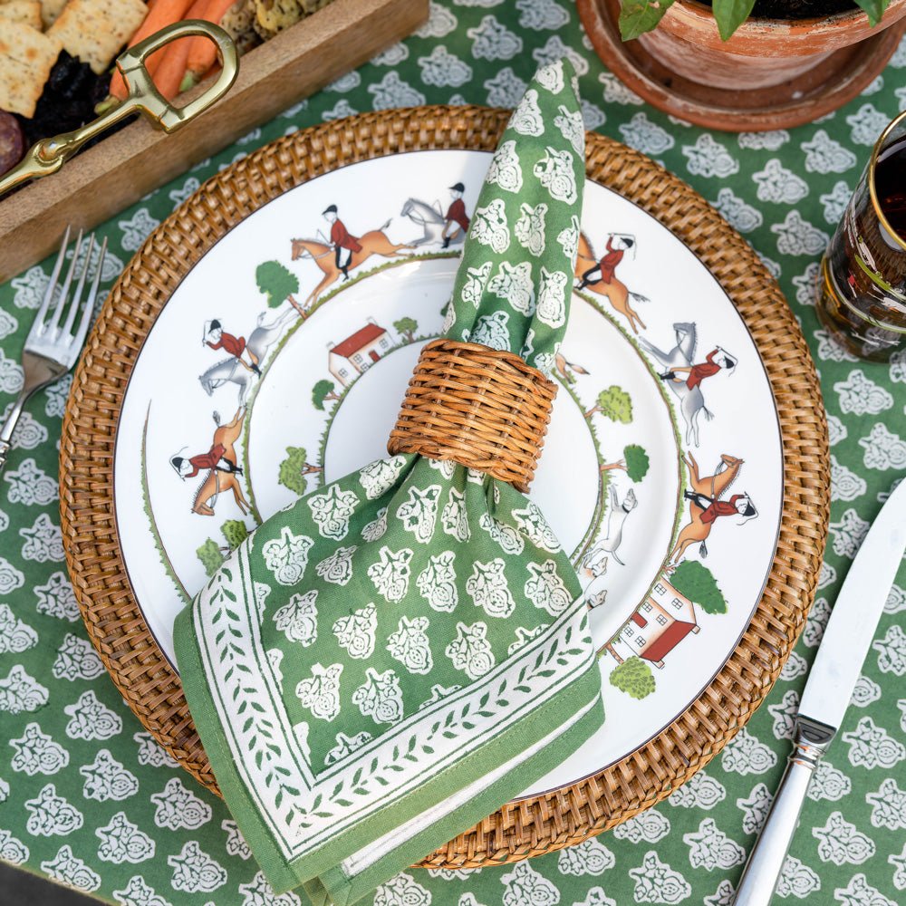 Pom Buti Green napkin with wicker napkin ring on plate and wicker charger on matching tablecloth