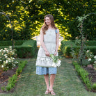 Model wearing apron and holding flowers. 