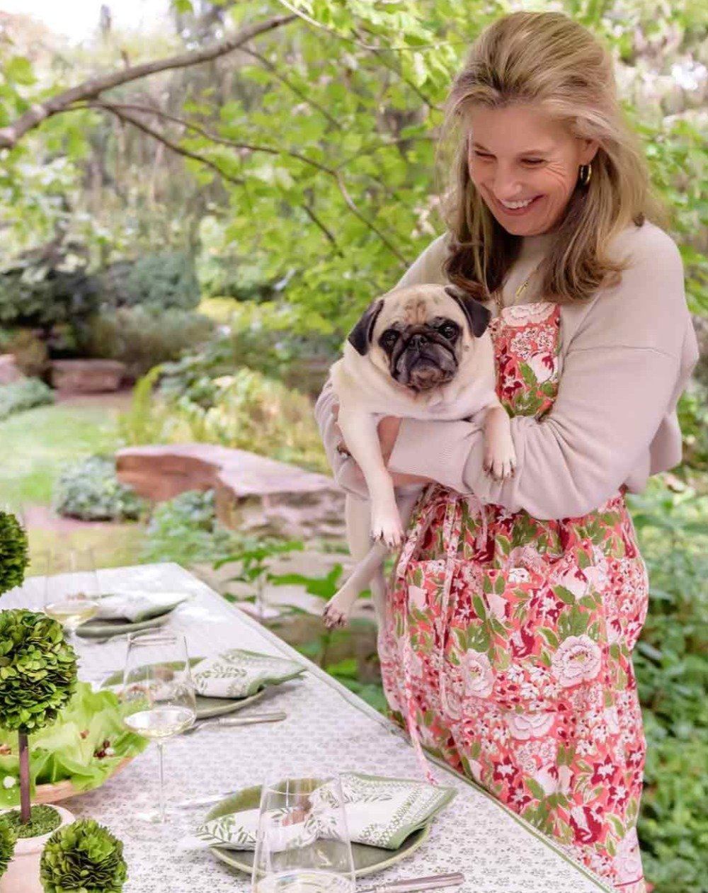 Woman holding dog in floral and fruit printed apron.